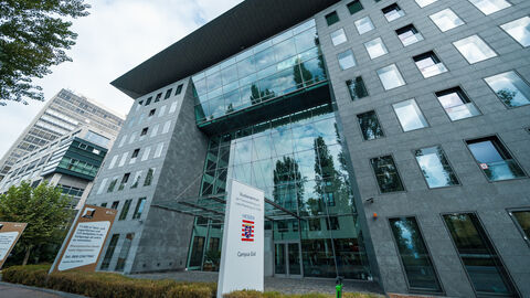 Eine große weiße Stele des Studienzentrums steht draußen vor dem Gebäude des Campus Süd.