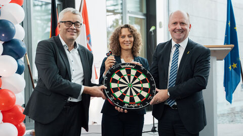 Die drei Personen halten eine Dartsscheibe.