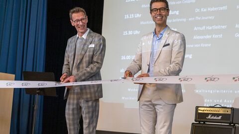 Zwei Männer schneiden mit einer Schere ein Band durch