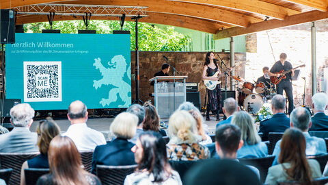 Publikum sehen auf einer Freiluftbühne eine Leinwand mit dem Hessenlöwen und eine 4 köpfige Band spielt