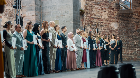 Diplom-Finanzwirtinnen und Diplom Finanzwirte halten auf einer Bühne ihre Diplome in der Hand.