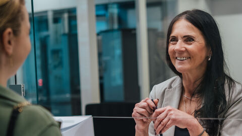 Eine Frau lächelt eine Anwärterin am Service-Schalter an.