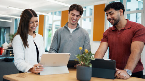 Eine Anwärterin und zwei Anwärter stehen um ein iPad herum.